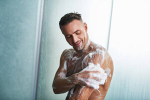 Waist up portrait of smiling naked gentleman with foam on his body taking shower at home